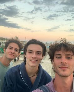 three young men standing next to each other at the beach