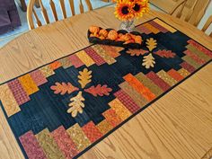 a quilted table runner with fall leaves and sunflowers in a vase on it