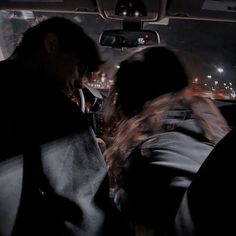 two people sitting in the passenger seat of a car at night with city lights behind them