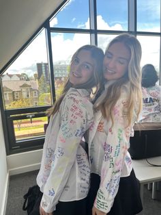 two young women standing next to each other in front of a window with writing on it