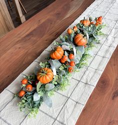 an arrangement of pumpkins and greenery is arranged on a white table runner in the kitchen