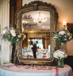 there is a mirror on the table with flowers in vases next to it that says hello gorgeous, you look incredible