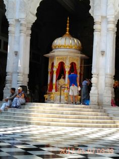 some people are sitting on the steps in front of a small building with columns and pillars