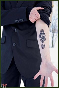 a person with a tattoo on their arm in the snow, wearing a black suit