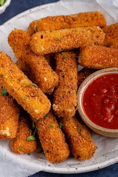 some fried food on a white plate with ketchup and sauce in a bowl