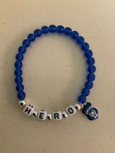 "Support your favorite police officer with this adorable HERO bracelet. Made with glass blue beads, and plastic letters surrounded by silver beads. There is a small enamel police badge charm hanging from the side.   It stretches to fits up to a 7.5\" wrist.  Comes wrapped in a gift giving bag with tie. In stock items ship within 2-3 business days.  Custom orders can take up to 10 days. Shipping Times - Please allow 3-5  delivery in the U.S.  7-10 business days to Canada and 10-15 business days t Personalized Blue Charm Bracelet With Round Beads, Blue Charm Bracelet With Letter Beads, Blue Charm Bracelet With Letter And Round Beads, Hero Bracelet, Police Bracelet, I Am A Hero, Beaded Charm Bracelet, Plastic Letters, Police Badge