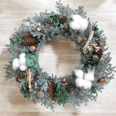 a christmas wreath with pine cones, cotton balls and greenery on a wooden surface