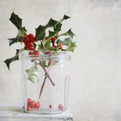 a glass jar filled with holly and berries