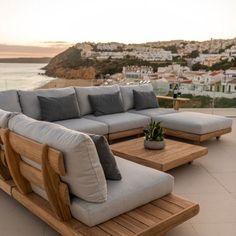 a couch and table sitting on top of a patio next to the ocean with buildings in the background