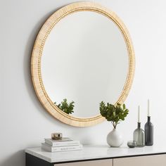 a round mirror sitting on top of a dresser next to a vase