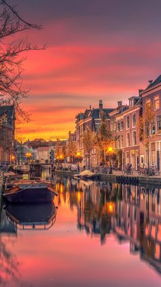 a boat is sitting in the water near some buildings and trees at sunset or dawn