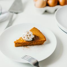 a slice of pumpkin pie on a plate with whipped cream and eggs in the background