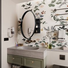 a bathroom with floral wallpaper and green vanity drawers, an oval mirror above the sink