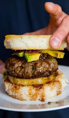 a person holding a hamburger on top of a white plate