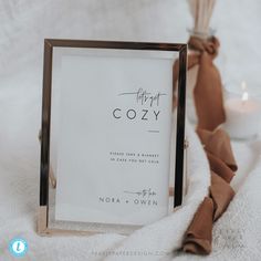 a sign that says happy cozy next to a candle on a white blanket with a brown ribbon