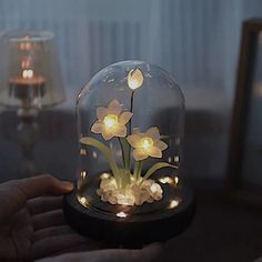 a glass dome with flowers in it on a table next to a person holding a lamp