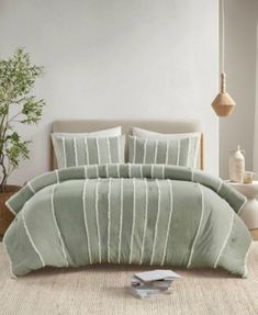 a bed with green comforter and pillows in a room next to a potted plant