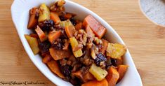 a white bowl filled with carrots and raisins on top of a wooden table