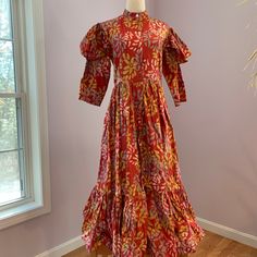 This Is A Never-Worn Sika Designs Brand Dress Made Of Beautiful 100% Cotton Batik Hand Made In Ghana. The Dress Has A Red Background, With Yellow, Gold And Blue Floral Design. The Sleeves Have An Interesting Fluttery Part Atop The Long Sleeve Itself, Making The Dress Look Victorian To Me. The Dress Buttons Down From The Mandarin Collar To The Flouncy Hem, And Has Side Seam Pockets, Plus A Sash. This Dress Has Volume, And Is A Uk Size 12. The Dress Is 50 In Long From Neckline To Hem; Please Double The Following: 15 In Waist, 17.5 In Pit To Pit, Hips Are Free Size Due To The Elegant Flare Of The Dress From The Waist. Red Long Sleeve Dress With Batik Print, Red Long Sleeve Dresses With Batik Print, Red Fitted Dress With Batik Print, Red Cotton Batik Print Dresses, Red Fitted Block Print Dress, Red Cotton Dress With Batik Print, Fitted Red Dress With Batik Print, Fitted Red Block Print Dress, Fitted Batik Print Dress For Spring