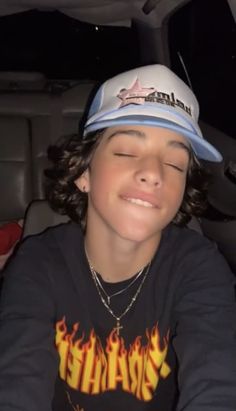 a young boy sitting in the back seat of a car wearing a hat with flames on it