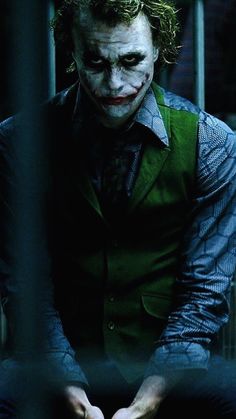 the joker is sitting behind bars in his caged - in area, looking at something