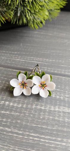 three white flowers are sitting on top of a wooden table next to a pine tree