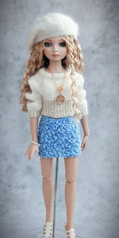 a doll with long blonde hair wearing a blue skirt and white sweater is standing in front of a gray background