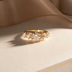 a three stone ring sits on top of a white cloth covered box with gold trim