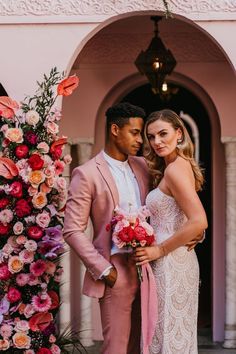 a man and woman standing next to each other in front of a flower covered archway