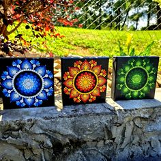 three small paintings are sitting on a stone ledge in front of a tree and fence