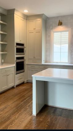 an empty kitchen with white cabinets and wood floors