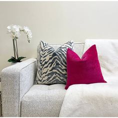 a white couch with two pillows on top of it next to a vase filled with flowers