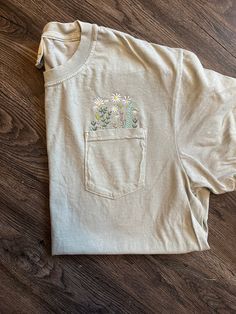 Wildflower Pocket T, the perfect decorative T for spring/summer! Spring Crew Neck Tops With Floral Embroidery, Spring Cotton T-shirt With Short Sleeves, Summer Cotton Floral Print T-shirt, Summer Crew Neck Tops With Floral Embroidery, Summer Floral Embroidery Relaxed Fit T-shirt, Spring Floral Embroidered Short Sleeve Tops, Casual T-shirt With Daisy Print For Spring, White Daisy Print T-shirt For Summer, Spring Relaxed Fit Short Sleeve T-shirt