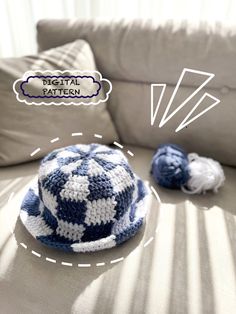 a blue and white crocheted hat sitting on top of a couch next to two balls of yarn