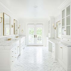 a white bathroom with marble counter tops and gold trimmings on the doors, windows, and double sinks