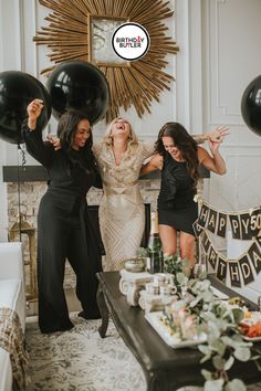 three women standing in front of a table with black balloons