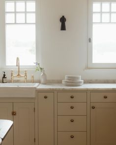 a kitchen with white cabinets and marble counter tops, two windows above the sink are gold faucets