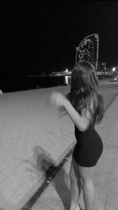 a woman in a black bathing suit standing on the beach at night with her arms behind her back