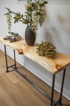 a wooden table topped with a vase filled with flowers next to a metal pipe leg