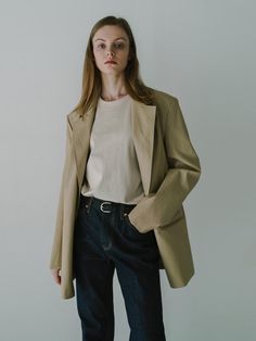 The individual is wearing an oversized blazer with a notched lapel, a contemporary take on classic suiting. The blazer has a single-button closure, which creates a streamlined and modern look. Its length extends to mid-thigh, offering a relaxed and stylish silhouette that could easily transition from office wear to casual settings. The fabric seems to have a smooth texture and a slight sheen, suggesting a blend that may include materials like viscose or silk.- The oversized fit is a nod to current trends, providing a comfortable yet chic aesthetic.- The neutral tone of the blazer makes it a versatile piece for layering over different outfits.- The simplicity of the design, with minimal visible detailing, gives this blazer a clean and sophisticated finish. Classic Everyday Blazer With Lapel Collar, Classic Blazer With Lapel Collar For Everyday, Classic Everyday Blazer With Hidden Button Closure, Classic Tailored Everyday Blazer, Classic Tailored Blazer For Everyday Wear, Tailored Blazer With Lapel Collar For Everyday, Elegant Everyday Blazer With Notch Lapel, Classic Tailored Blazer, Everyday Tailored Single Breasted Blazer