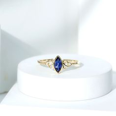 a gold ring with a blue stone sitting on top of a white stand next to a bottle