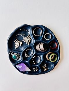 a black tray with rings and earrings in it on a white surface next to a purple flower