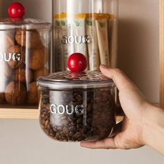 a person holding a jar with nuts in it next to other jars and containers on the shelf