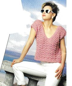 a woman sitting on top of a stone bench wearing white pants and a pink sweater