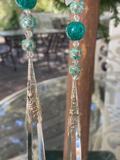 two green and clear crystal earrings hanging from a tree branch in front of a glass table