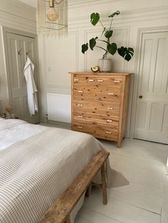 a bed room with a neatly made bed and a plant on top of the dresser