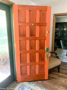 an orange door with green knobs in a living room next to a chair and window