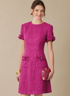 a woman in a bright pink dress and gold accessories smiles at the camera while holding a purse