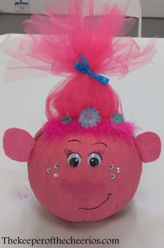 an orange pumpkin with pink hair and blue flowers on it's head is sitting on a table