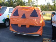 a woman standing next to a car with a pumpkin costume on it's trunk